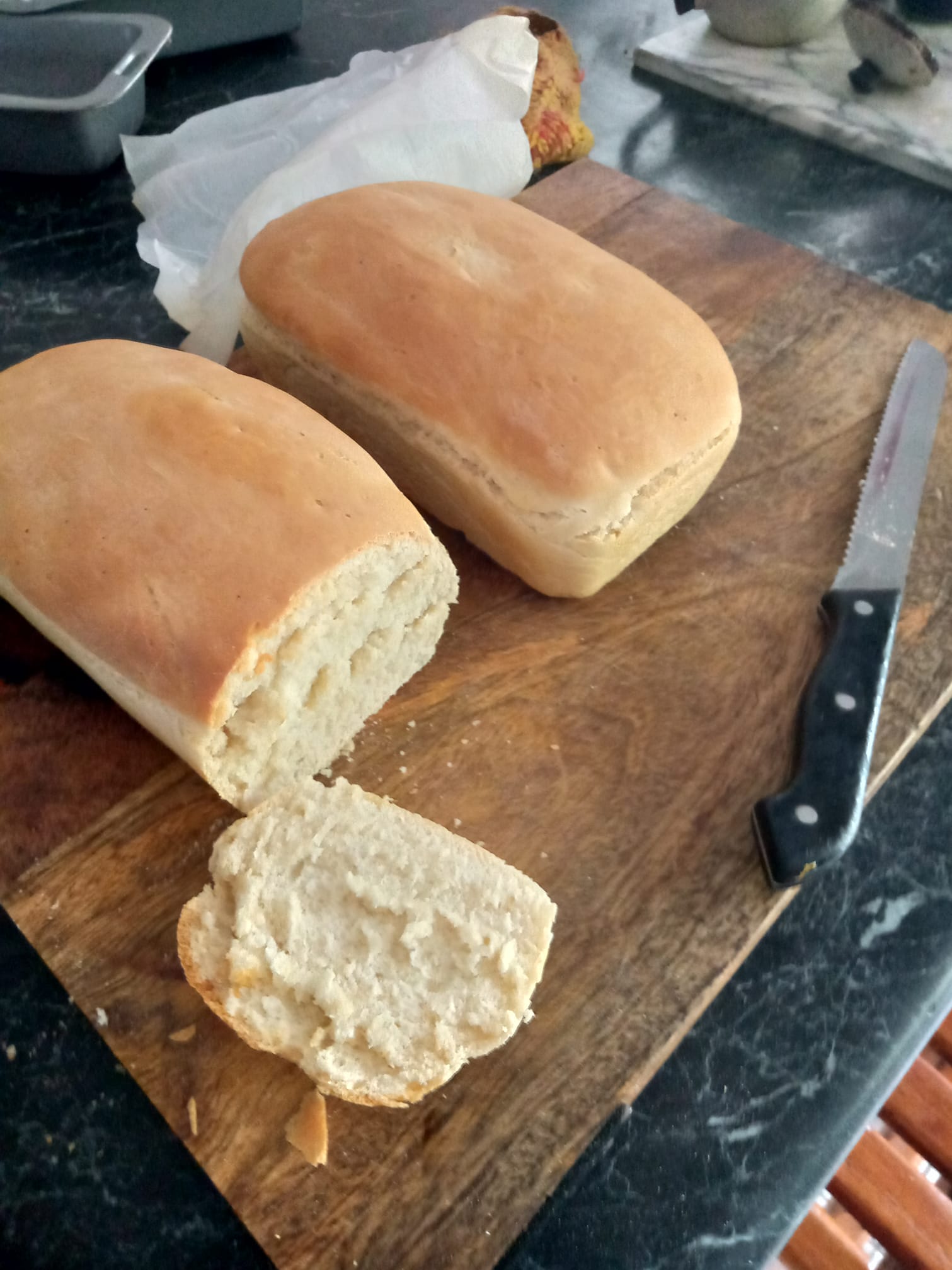 Image of two loaves of freshly baked next to a serrated knife. One loaf has been cut to show its inside